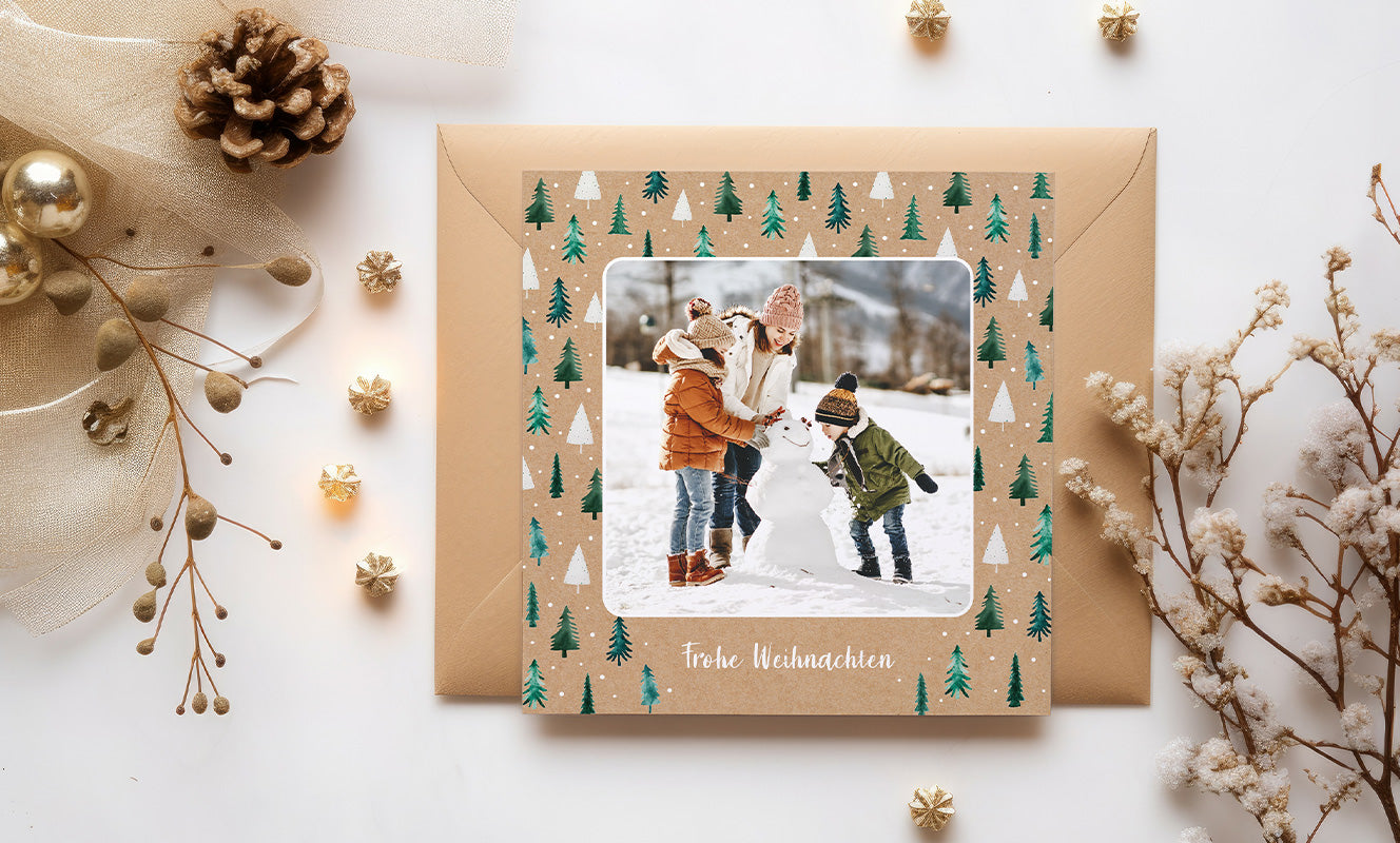 Einfache, quadratische, kraftpapierfarbene Weihnachtskarte mit vielen kleinen, in Wasserfarben gezeichneten Tannenbäumen im Hintergrund, einem quadratischen Foto mit abgerundeten Ecken in der Mitte und dem Text „Frohe Weihnachten“ darunter.